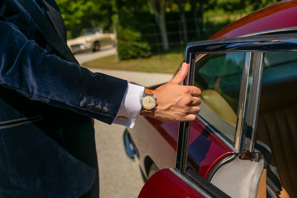 Gloved hand on the door of a classic car, a wristwatch visible at the cuff