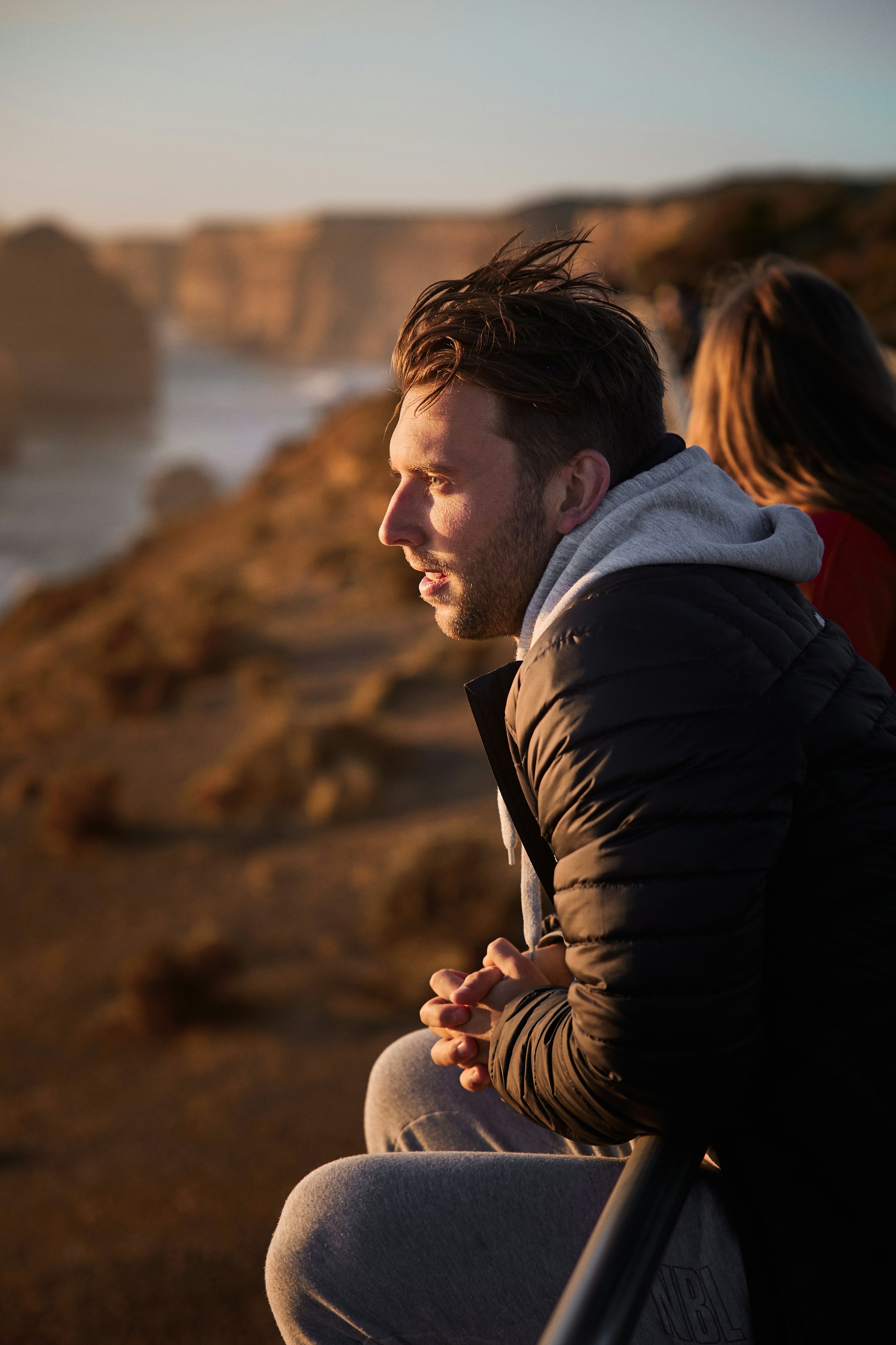 man in black jacket holding woman in red shirt near body of water during daytime