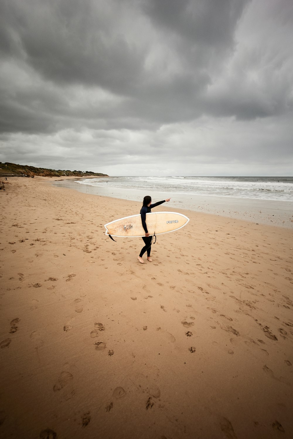 Person mit weißem Surfbrett, die tagsüber am Strand spazieren geht