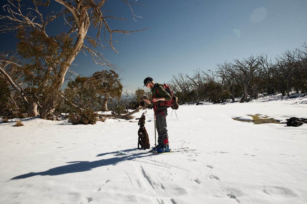 man in red jacket and black pants standing on snow covered ground during daytime