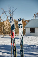 Close-up of ski boots and poles resting on snow beside a mountain lodge.