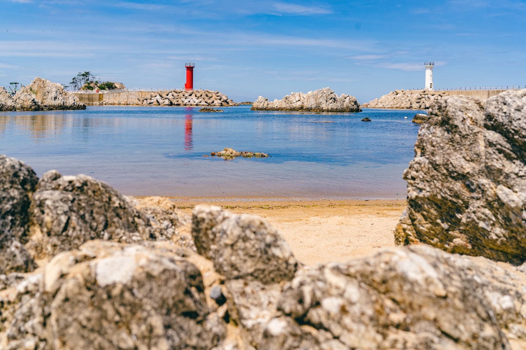 white and red lighthouse on gray rocky shore during daytime