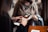 Two people are engaged in a transaction, with the focus on a hand holding a smartphone displaying an application. The background shows another person wearing a mask and holding a piece of clothing, suggesting an indoor setting.
