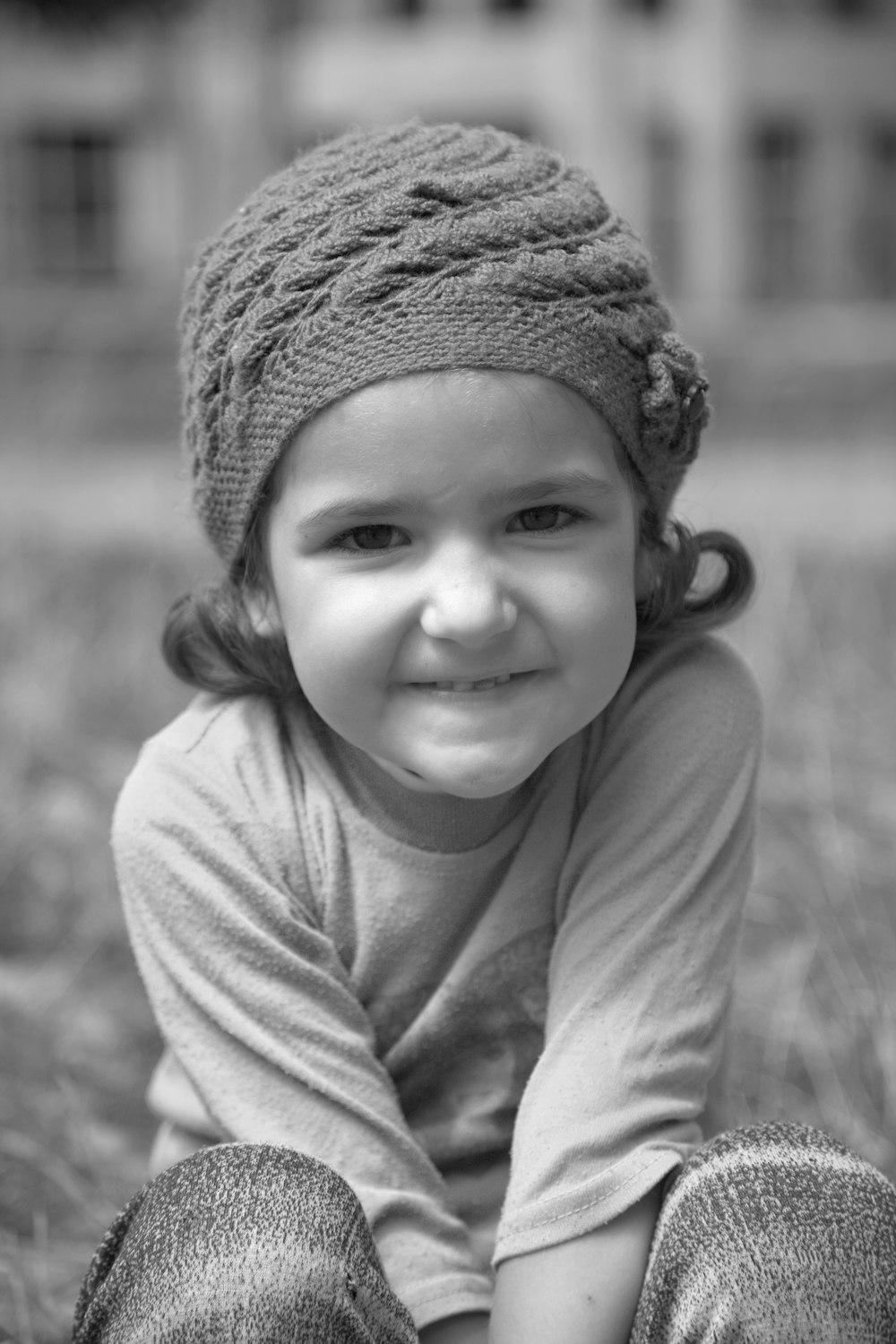 Foto en escala de grises de una chica sonriente con gorro de punto y camisa de manga larga con cuello redondo