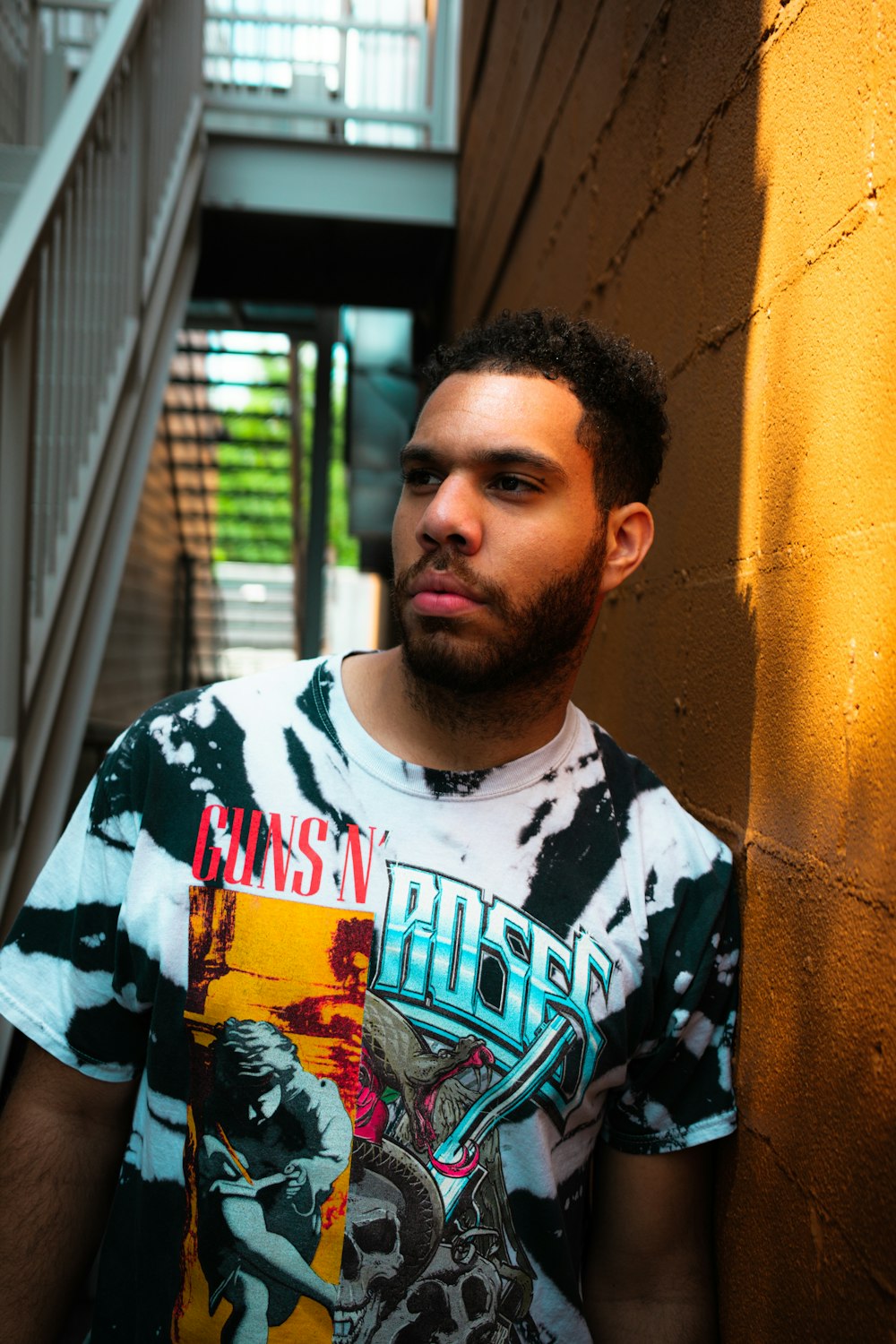 man in white and black crew neck t-shirt standing beside yellow concrete wall