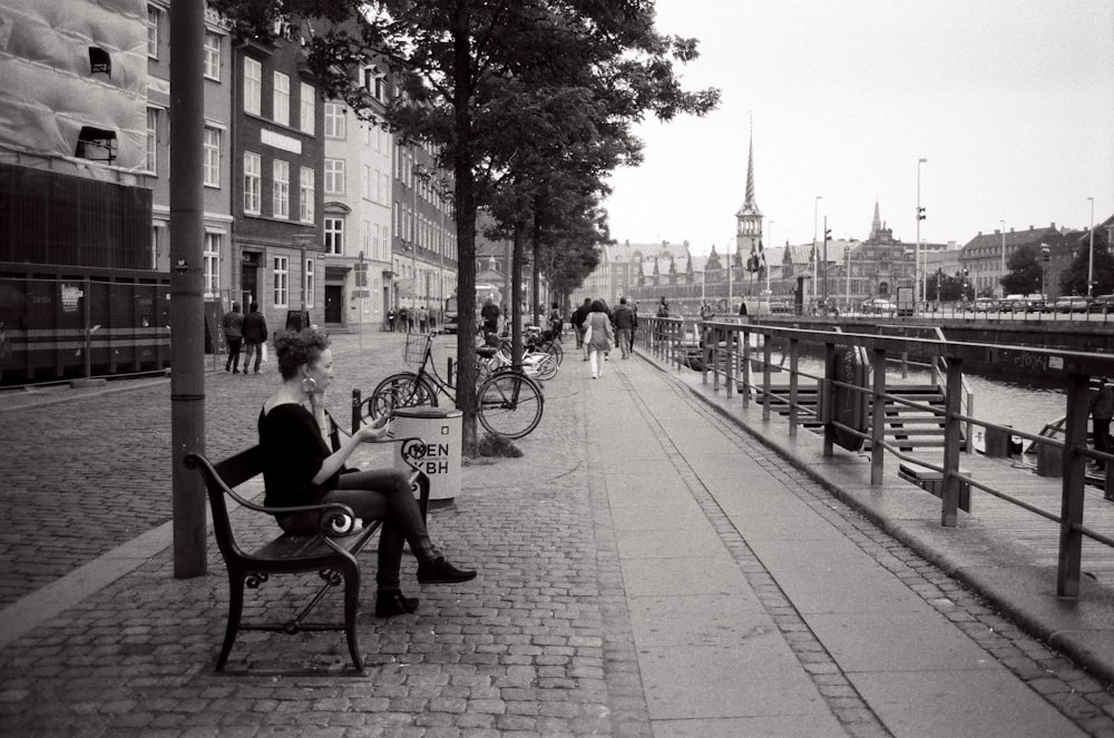 grayscale photo of person sitting on bench near bare trees