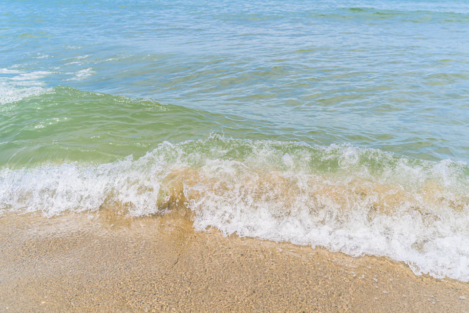 Serene beach scene with beige sand and turquoise water, waves crash against the shore