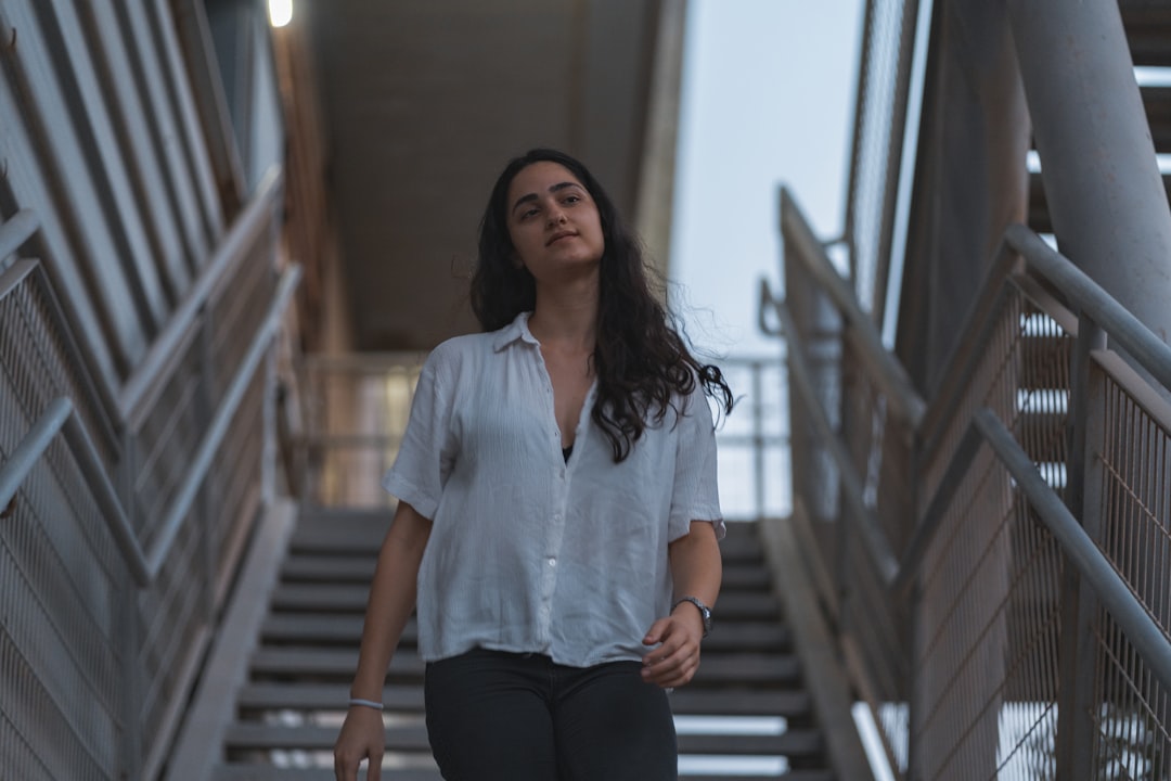 woman in white button up shirt and black pants standing on brown wooden stairs