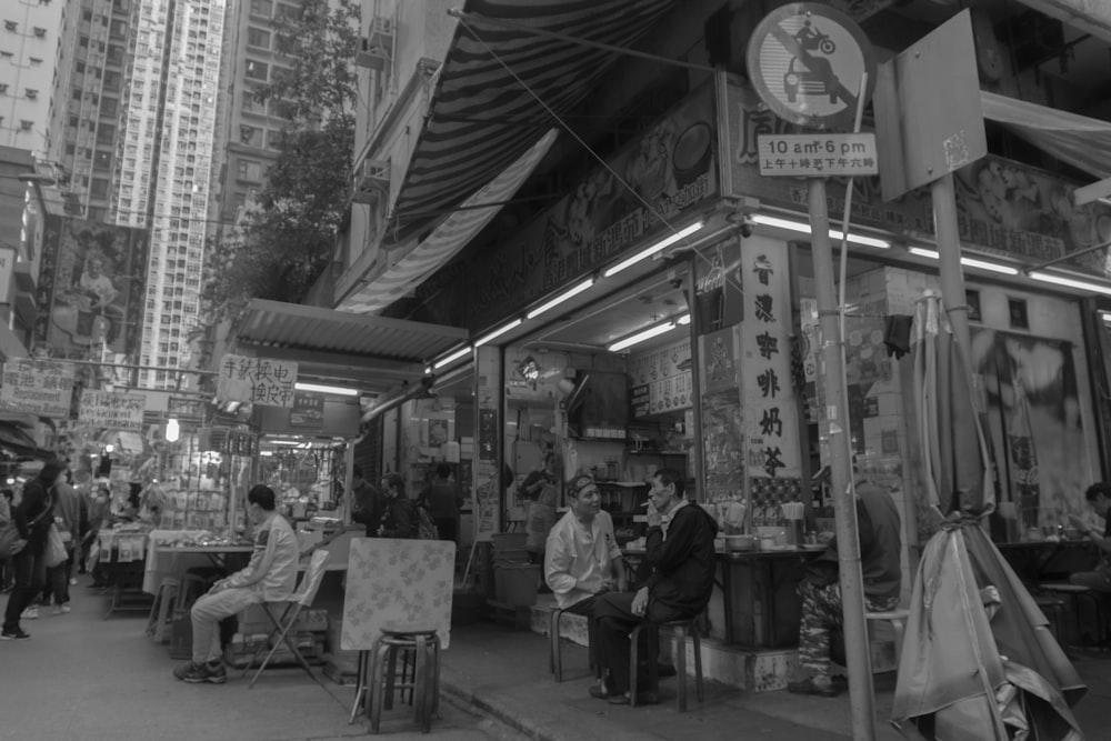 grayscale photo of people sitting on chair near store