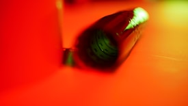 A close-up, abstract image featuring a rolled-up film or similar object with a reddish hue. The lighting creates a contrast between the saturated colors, giving a sense of depth and focus on the central object.
