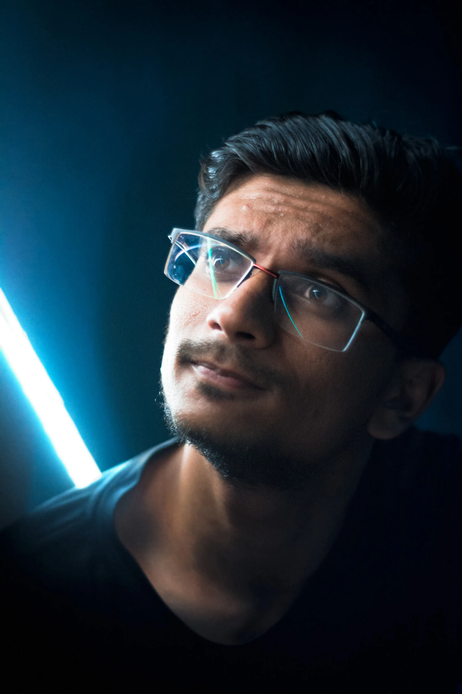 A man in angular dark frames lit from the side by a strip of blue light