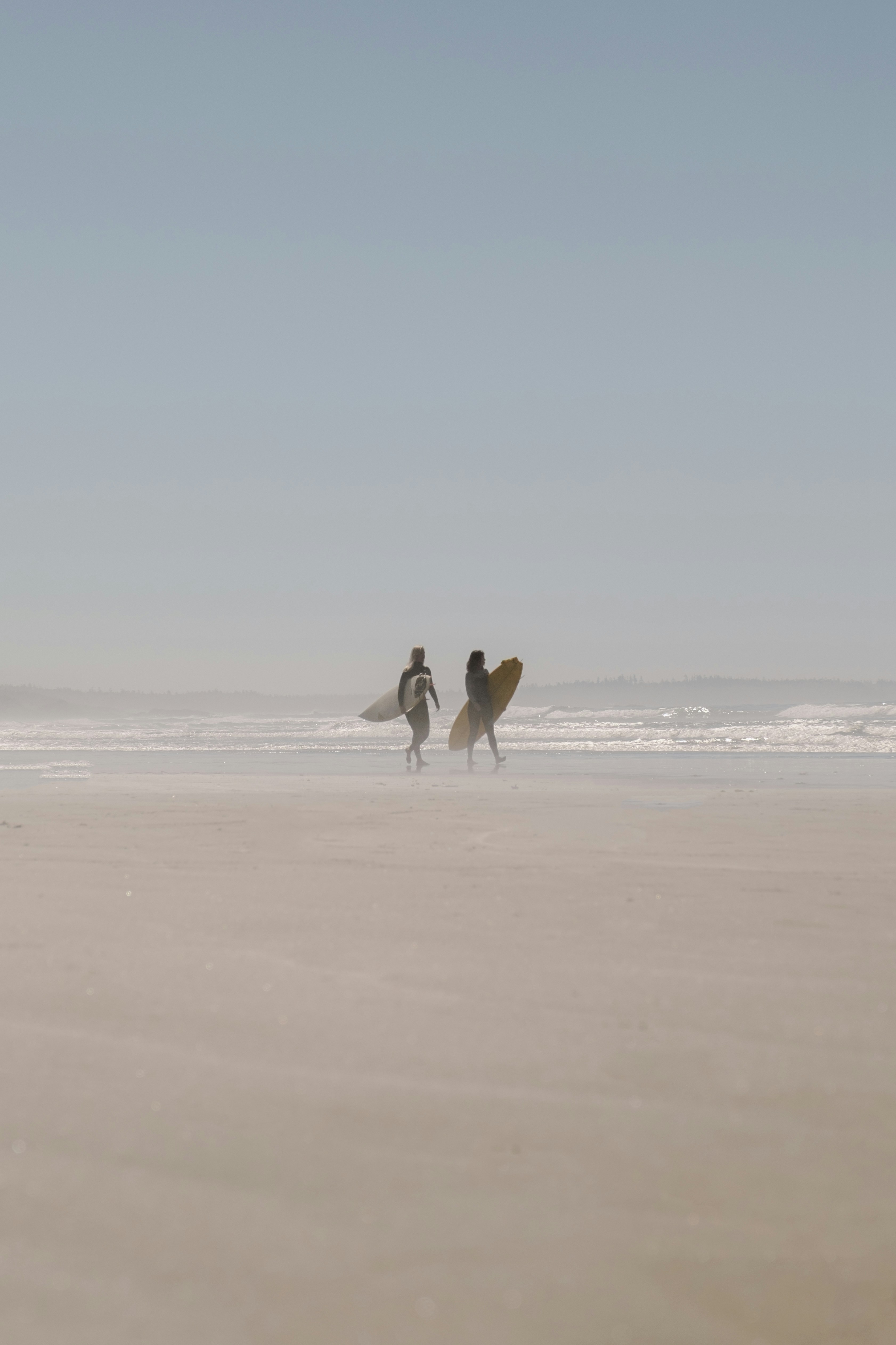 man in white shirt and black pants holding white surfboard walking on beach during daytime