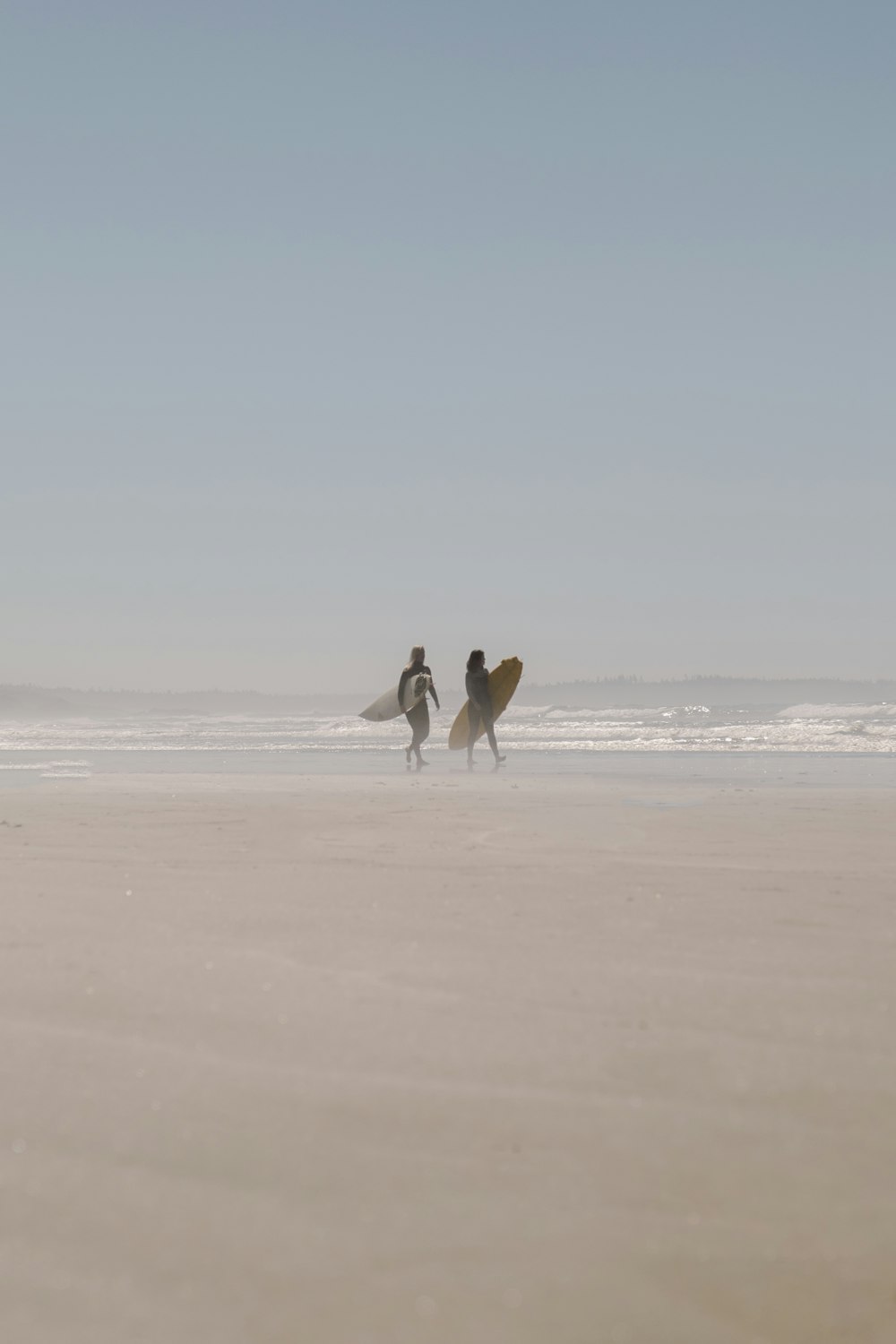 man in white shirt and black pants holding white surfboard walking on beach during daytime