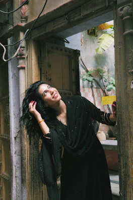 A smiling woman wearing a chic, modern dress with subtle Moroccan motifs, standing near a traditional door.