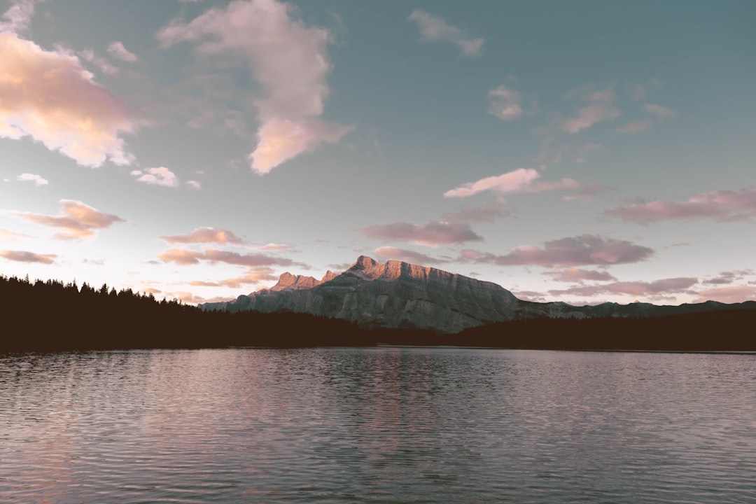 body of water near mountain under cloudy sky during daytime