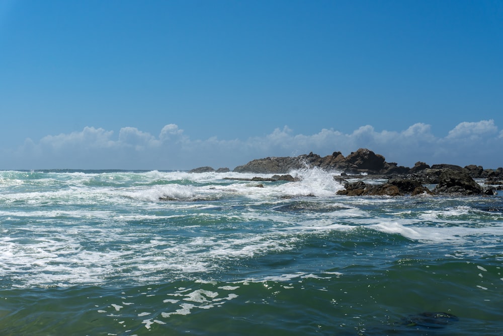 ocean waves crashing on rocky shore under blue sky during daytime