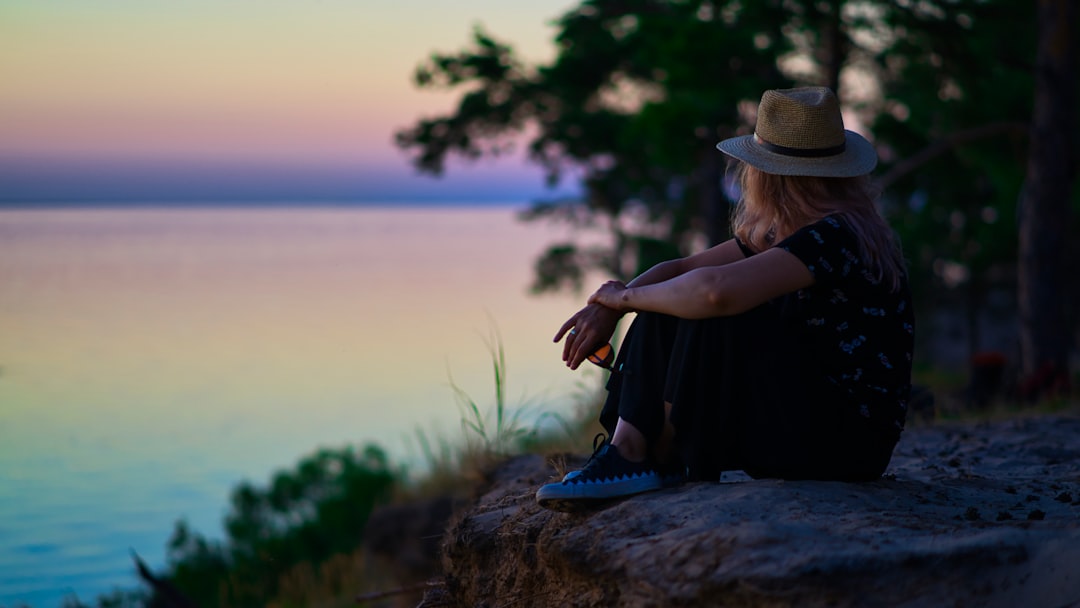 woman in black shirt and blue denim jeans sitting on rock near body of water during