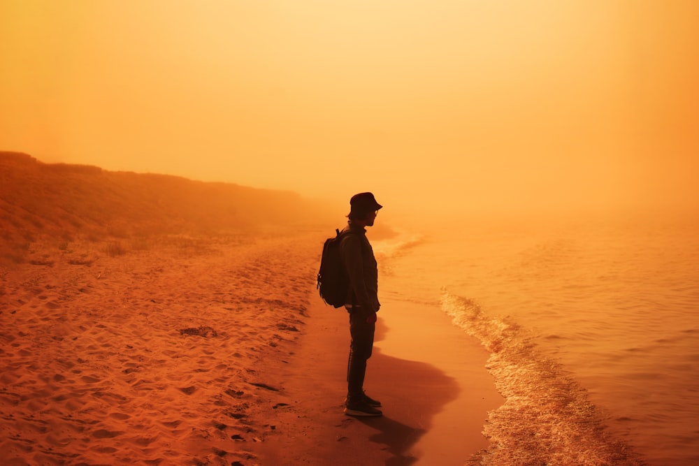 homem na jaqueta preta de pé na areia marrom durante o pôr do sol