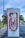 A series of Tesla electric vehicle superchargers are lined up in a visually appealing manner, creating a sense of depth and repetition. The background includes trees and a banner for the Arlington Expo Center.