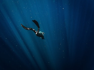 A serene underwater scene with a lone freediver gracefully descending into deep blue water.
