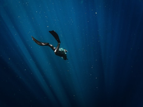 A serene underwater scene with a lone freediver gracefully descending into deep blue water.
