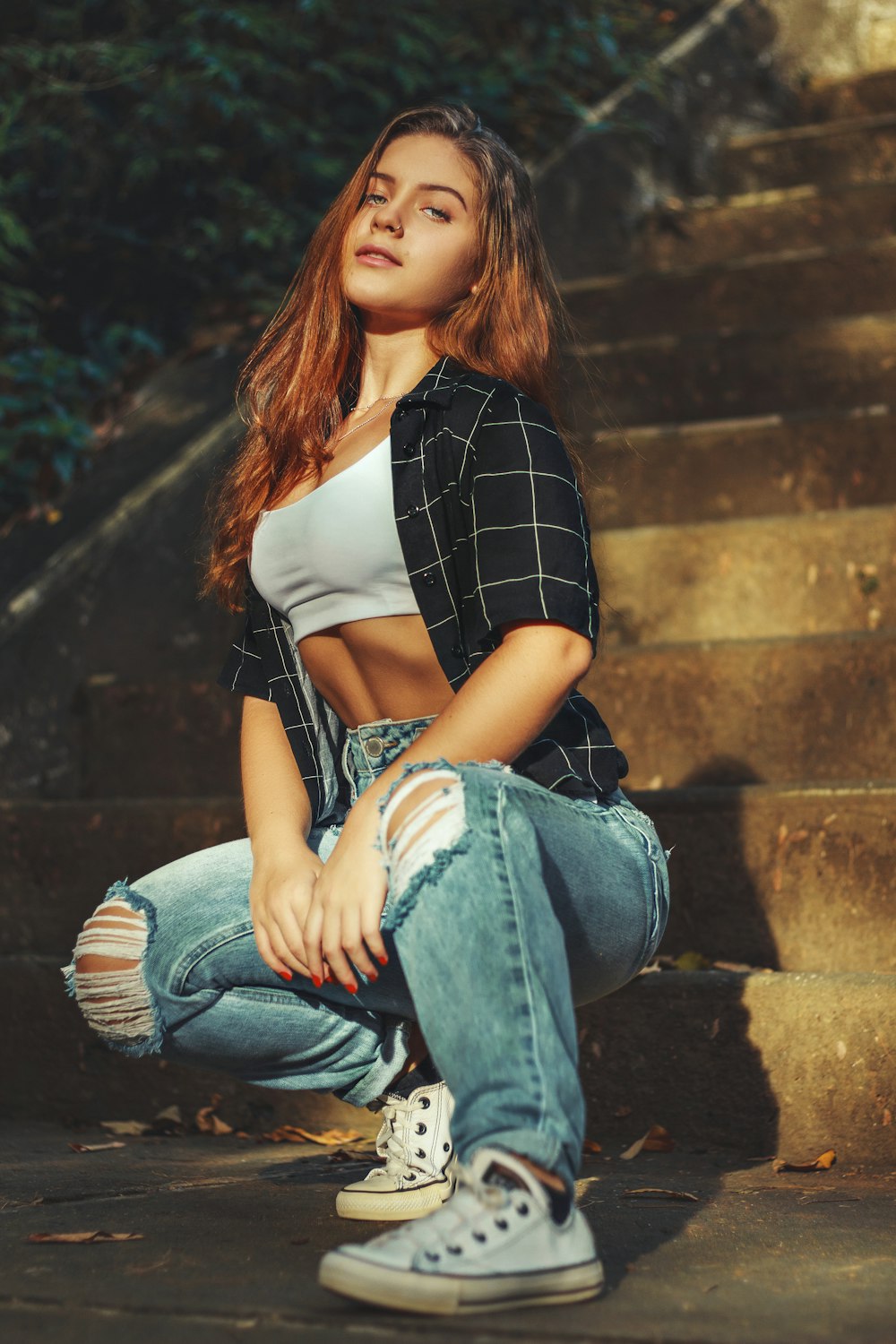 woman in black and white checkered shirt and blue denim jeans sitting on brown concrete stairs