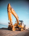 yellow excavator on gray rock near body of water during daytime