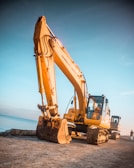 yellow excavator on gray rock near body of water during daytime