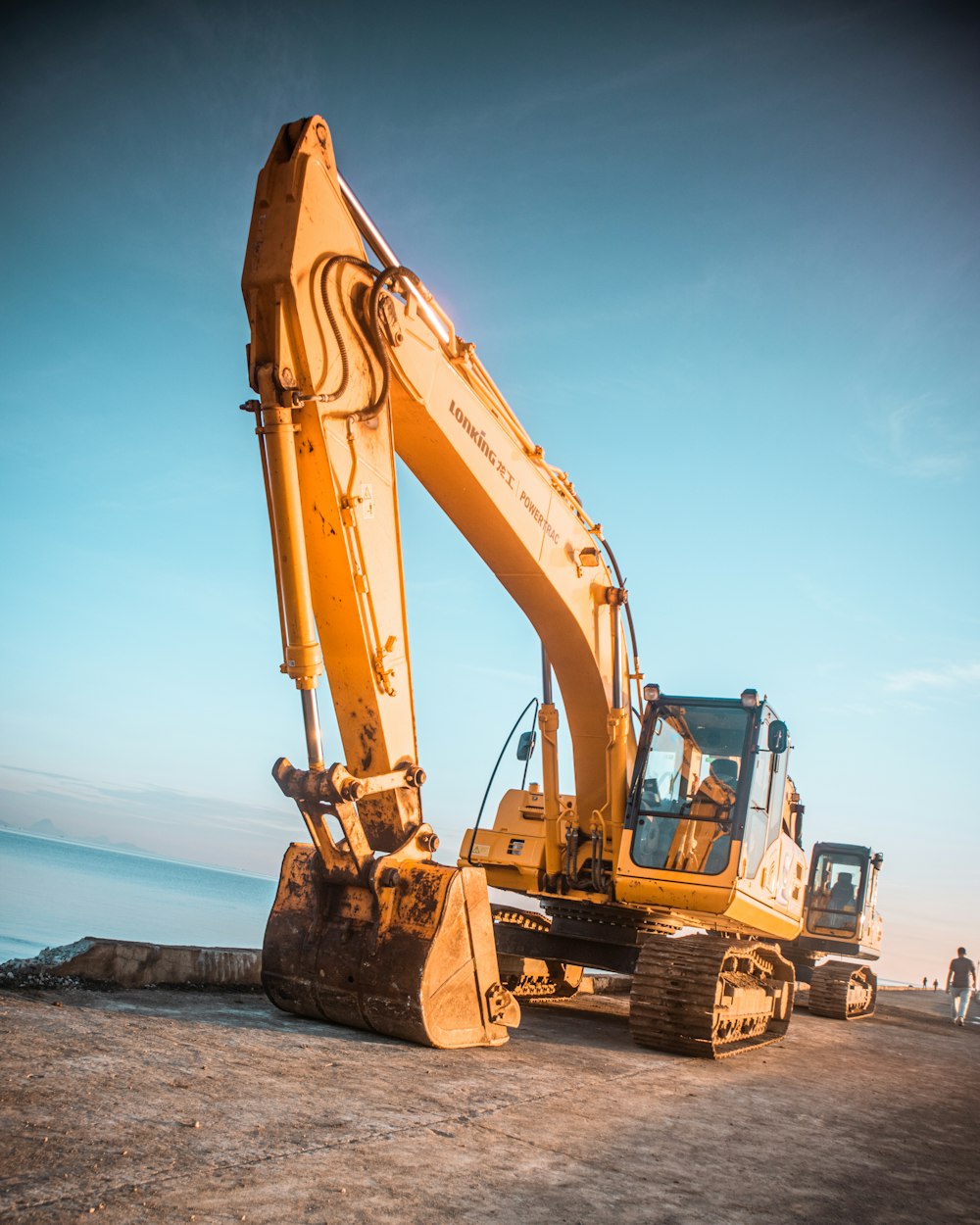 yellow excavator on gray rock near body of water during daytime