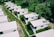 Aerial view of a series of small, white, rectangular houses with flat roofs arranged in rows. These homes are surrounded by lush greenery and grass-covered paths. Solar panels are visible on some of the rooftops.
