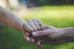 Close-up of intertwined hands with wedding rings in a sunlit garden.