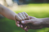 Close-up of intertwined hands with wedding rings in a sunlit garden.