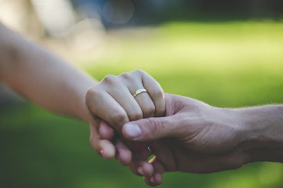 Elegant couple holding hands adorned with delicate wedding rings in a lush garden setting at sunset.