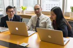 man in white dress shirt sitting beside woman in black blazer using macbook