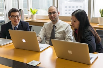 man in white dress shirt sitting beside woman in black blazer using macbook