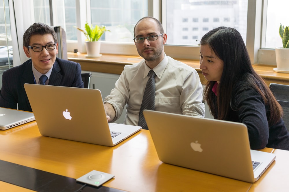 man in white dress shirt sitting beside woman in black blazer using macbook