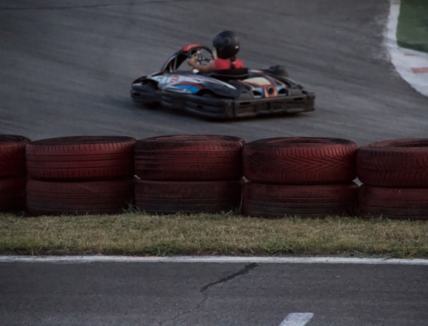 Close-up of a Pilott Racing go-kart speeding around a sharp corner, orange and black colors vivid under the sun.