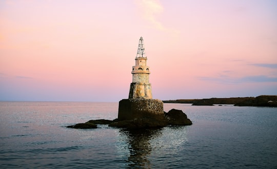 white and black lighthouse on rock formation beside sea during daytime in Ahtopol Bulgaria