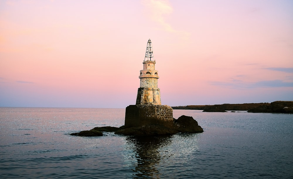 white and black lighthouse on rock formation beside sea during daytime