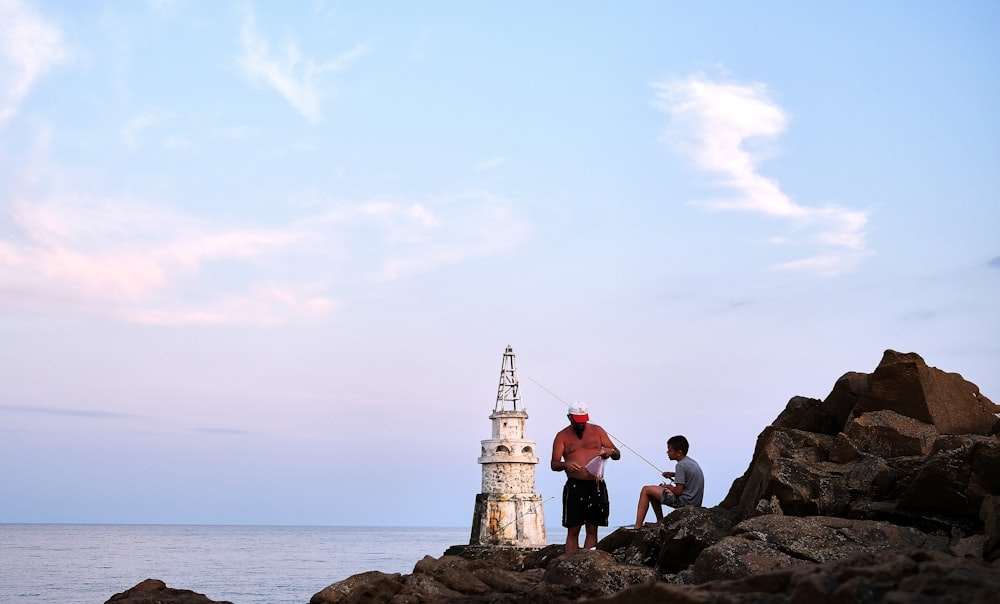 man in red shirt standing on rock formation near body of water during daytime