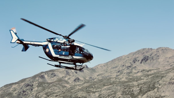 red and black helicopter flying over brown mountain during daytime