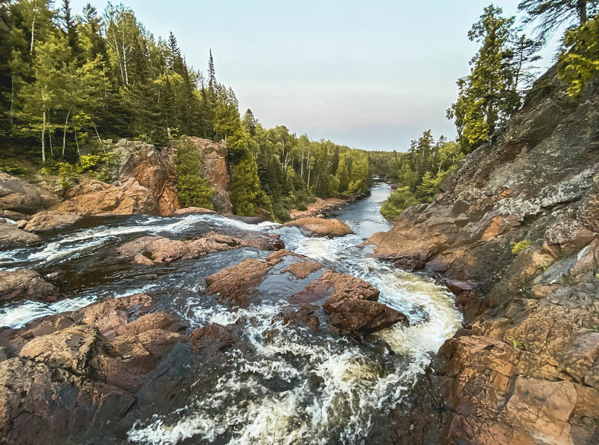 A river spilling over red rock ledges between forested banks in Tettegouche State Park