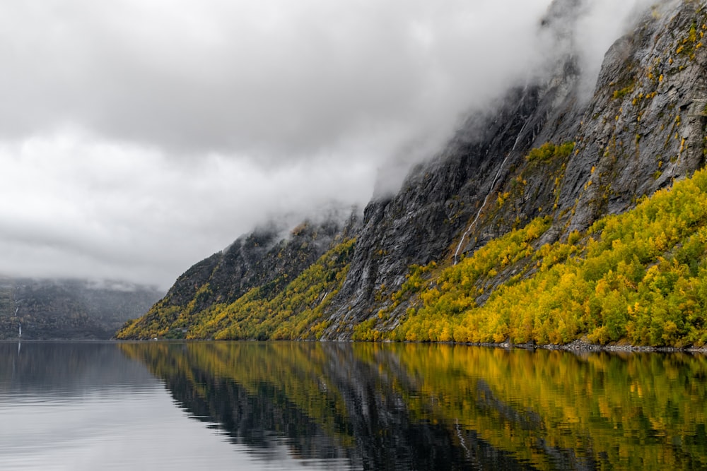 green and brown mountain beside body of water under cloudy sky during daytime