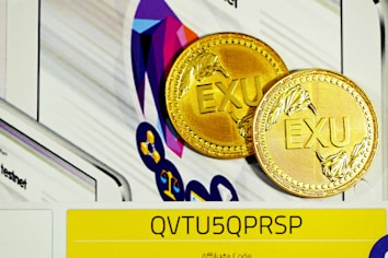 Two gold coins with the letters 'EXU' embossed on them are placed against a colorful, abstract geometric background. In the foreground, a yellow strip with the code 'QVTU5QPRSP' is visible, possibly indicating an affiliate or promotional code.
