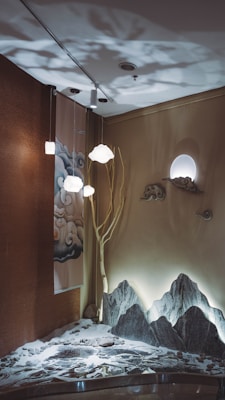 A serene indoor setup features an artistic wall design with subtle lighting. A tree branch extends toward the ceiling, surrounded by decorative clouds and a moon-like light source. The floor area presents an elaborate Zen garden with rocks and sand art, adding to the tranquil ambiance.