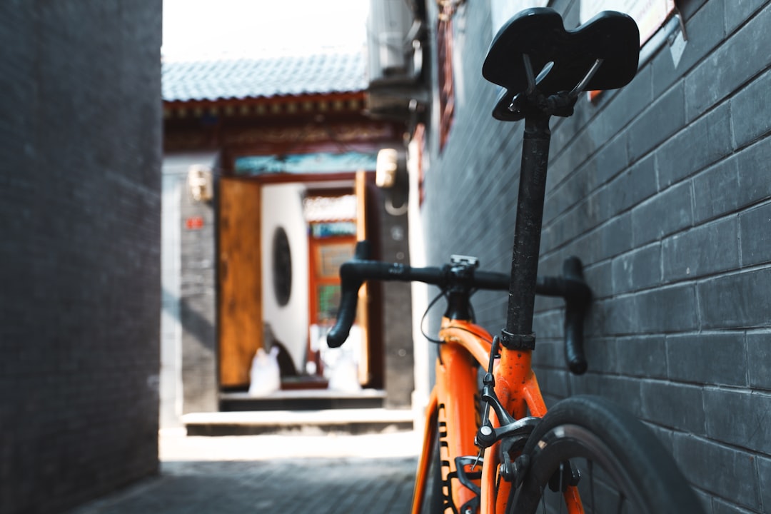 orange and black bicycle parked beside brown concrete building during daytime