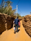 man in red shirt and blue denim jeans walking on brown dirt road during daytime