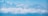 A panoramic view featuring a bright, blue sky with fluffy clouds partially covering rugged mountain peaks. A paraglider with a red and black parachute is soaring above the clouds, creating a sense of adventure.