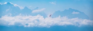 A panoramic view of paragliders soaring above lush valleys under a bright blue sky