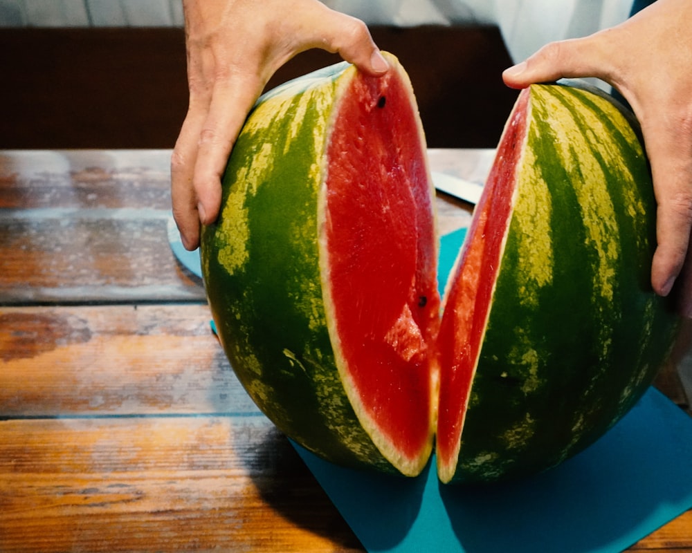 person holding watermelon on brown wooden table